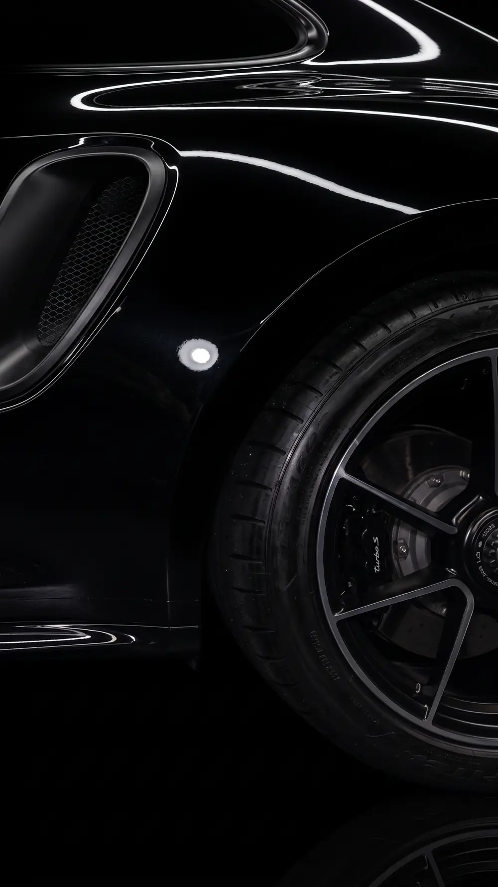 Close-up of the glossy black rear wing of a Porsche 911, with a long light reflected sharply in the paint.