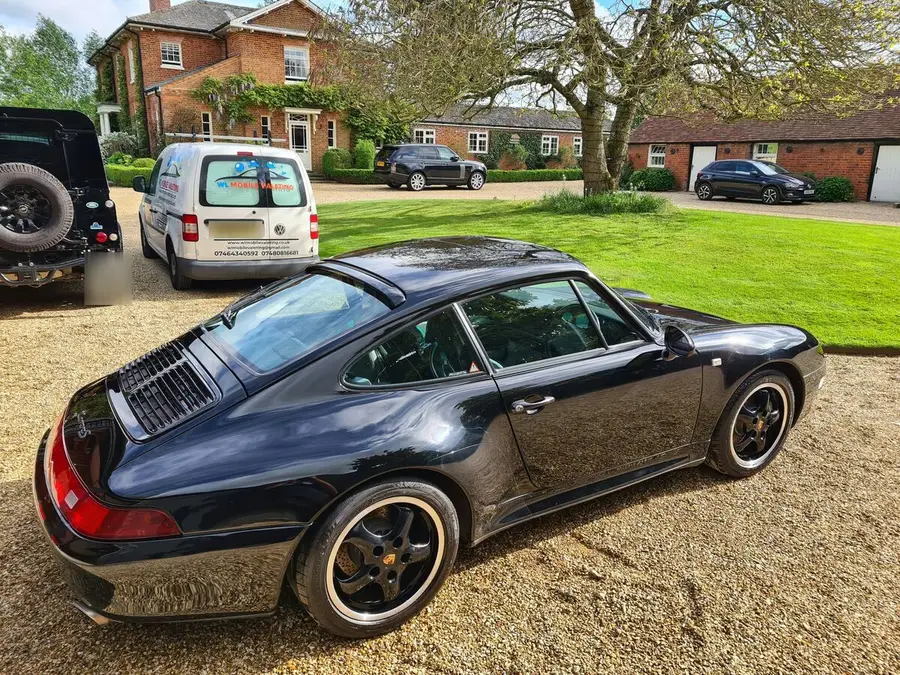 Black Porsche 911 coupé on a gravel drive, the WL van behind it.