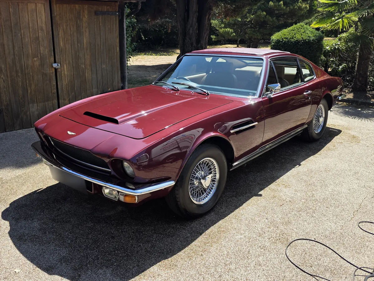 Maroon Aston Martin V8 parked outside a barn garage.