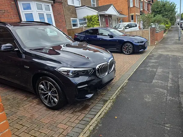 Black BMW X5 parked on a street, a blue BMW i4 behind it.