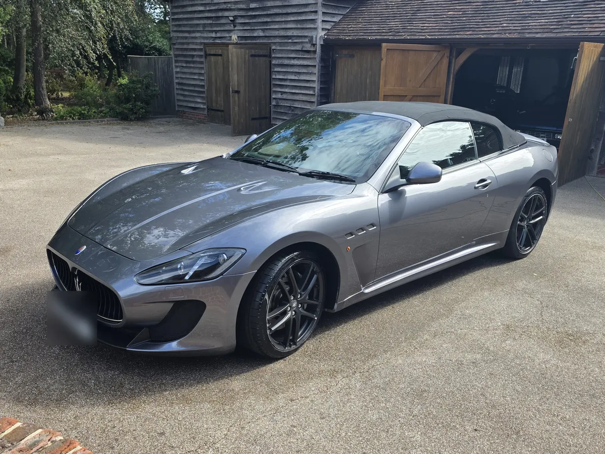 A grey Maserati convertible with its black soft top up, parked on a gravel driveway after a valet.