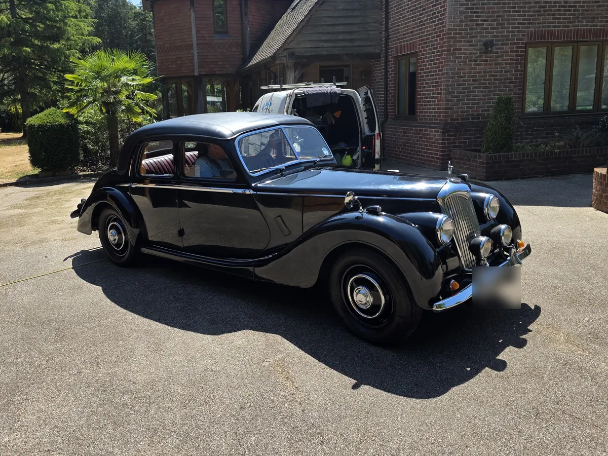 A black classic four-door saloon with a chrome grille and spot lamps, parked on a driveway after a valet.