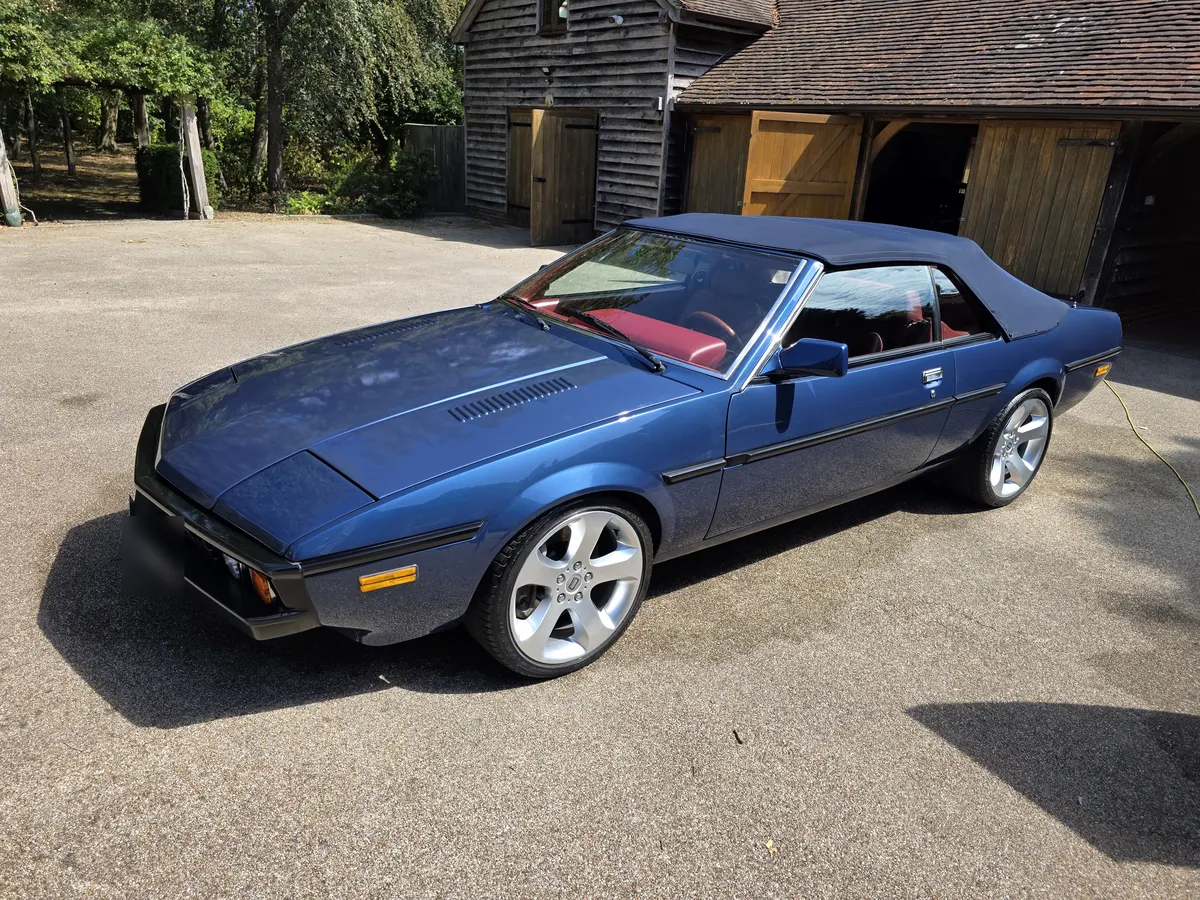 A blue classic convertible with a red interior and black soft top, parked on a driveway after a valet.