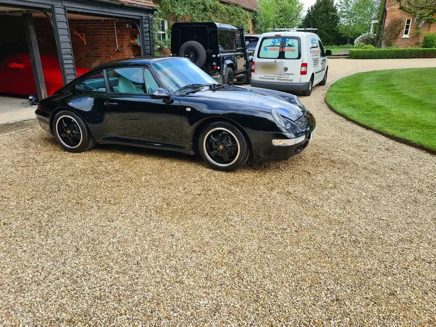 A black classic Porsche 911 on a gravel drive beside a garage after a valet.
