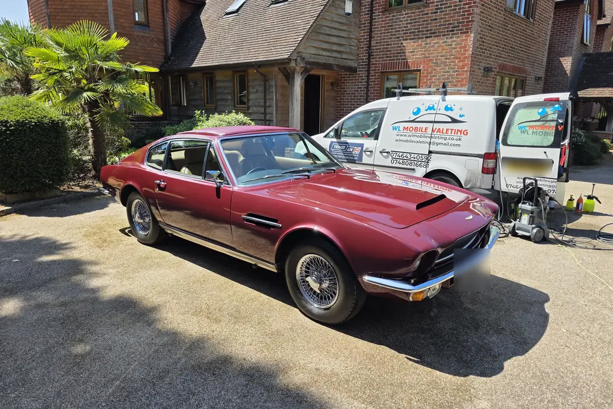 A maroon classic Aston Martin V8 on a driveway after a valet, with the WL Mobile Valeting van and pressure washer behind.