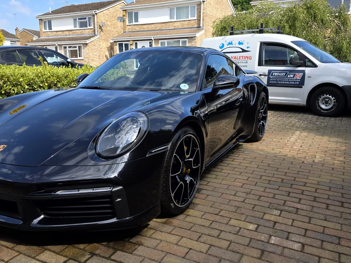 Front three-quarter view of a dark blue Porsche 911 after a valet, with the WL Mobile Valeting van alongside.