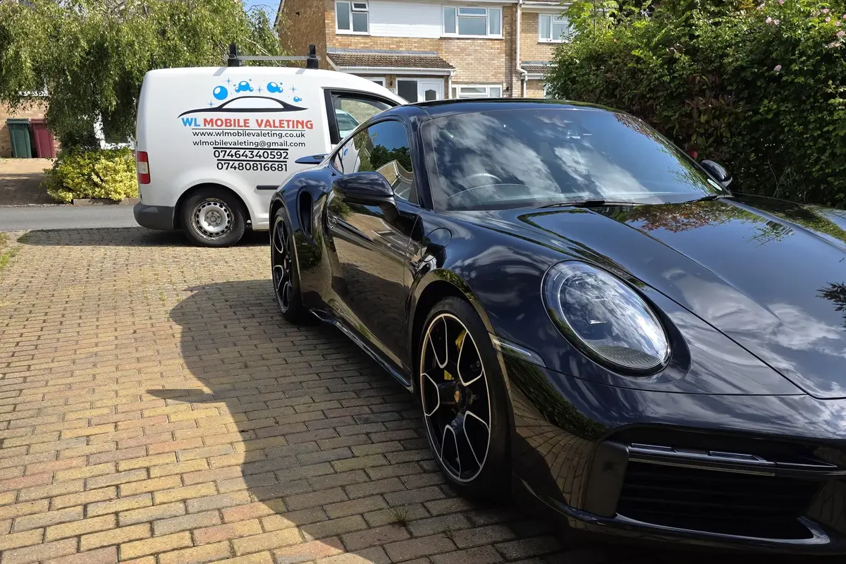 A freshly valeted dark blue Porsche 911 on a block-paved driveway, with the WL Mobile Valeting van parked behind it.