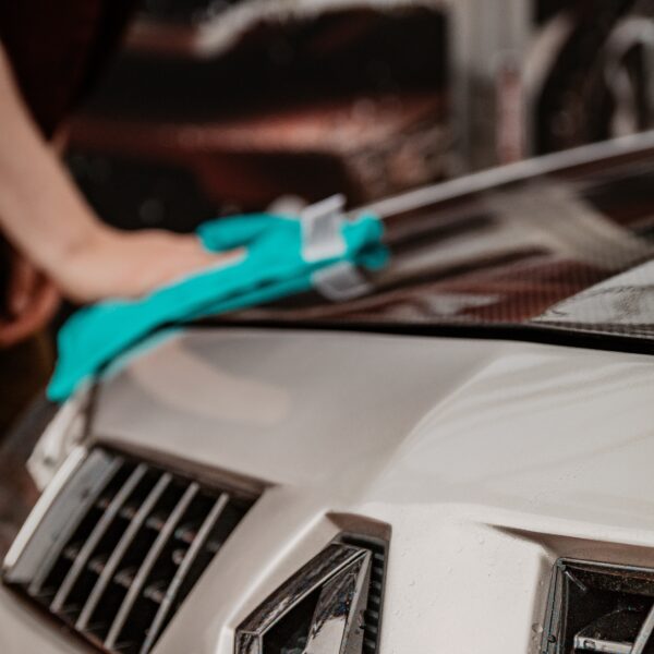 Someone cleaning the bonnet of a silver car with a green cloth