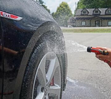 Side of a black car show the wheel being washed with a hose.