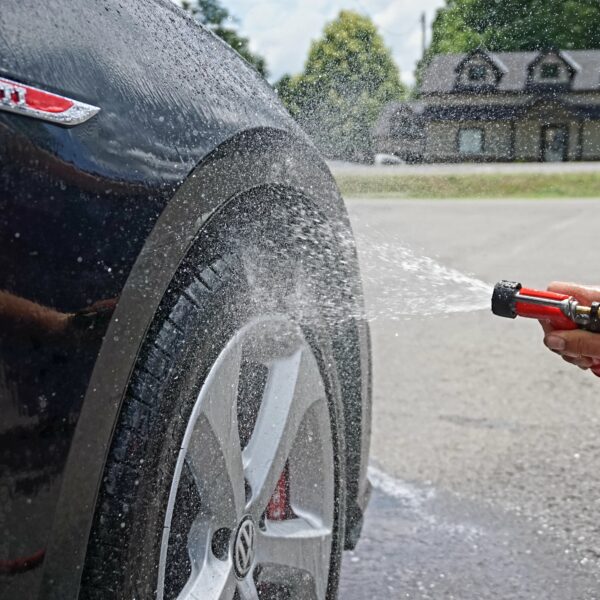 Side of a black car show the wheel being washed with a hose.