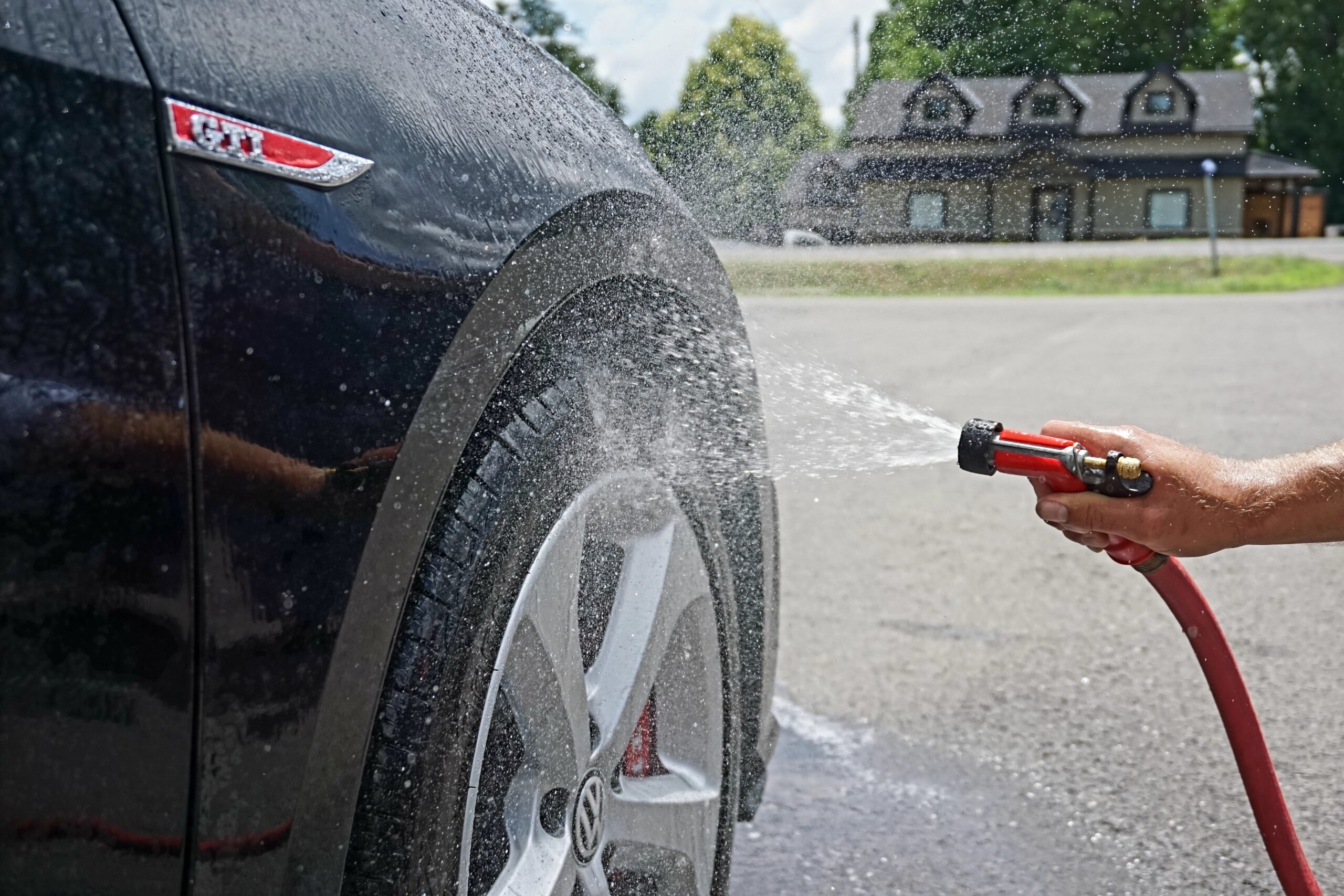 Side of a black car show the wheel being washed with a hose.