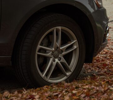 Wheel of a dark car surrounded by orange autumn leaves