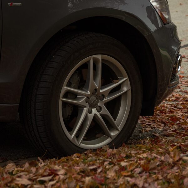 Wheel of a dark car surrounded by orange autumn leaves