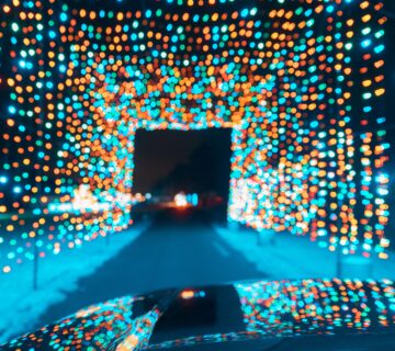 A tunnel of multicoloured lights over a road reflecting off the bonnet of a car driving through after a mobile valeting service.