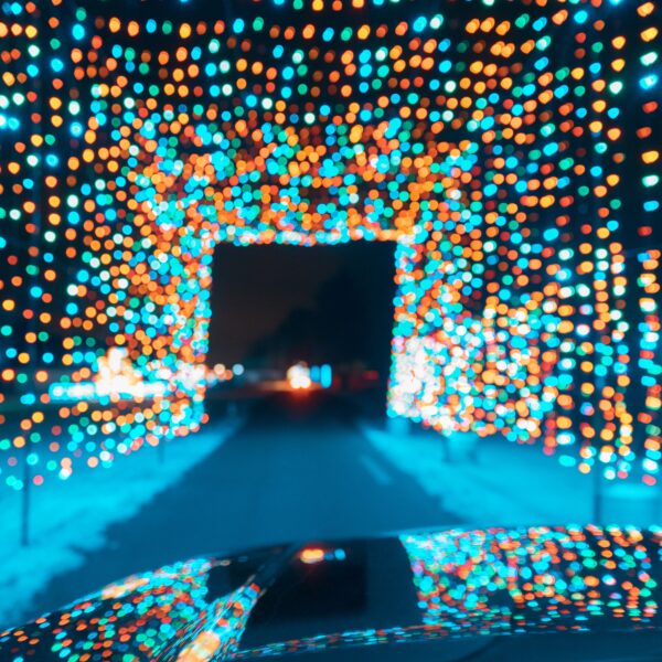 A tunnel of multicoloured lights over a road reflecting off the bonnet of a car driving through after a mobile valeting service.