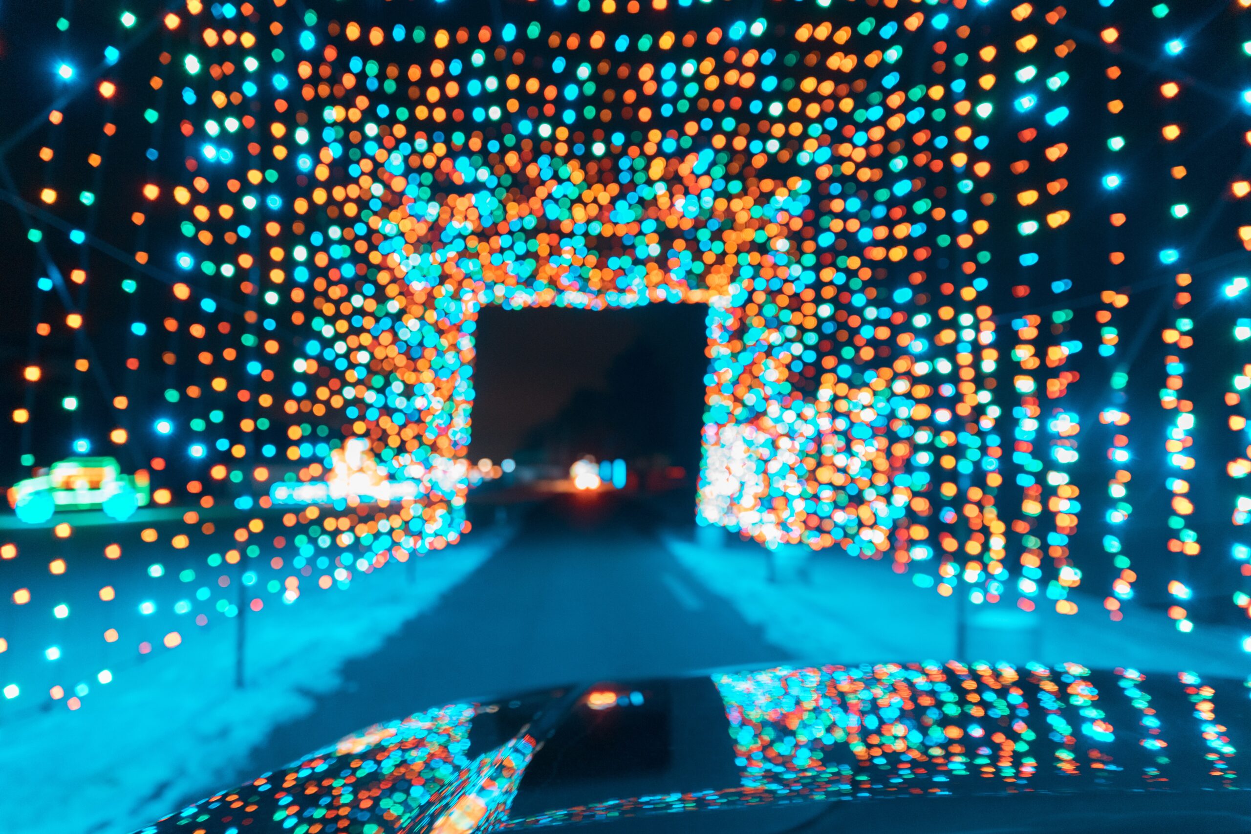 A tunnel of multicoloured lights over a road reflecting off the bonnet of a car driving through after a mobile valeting service.