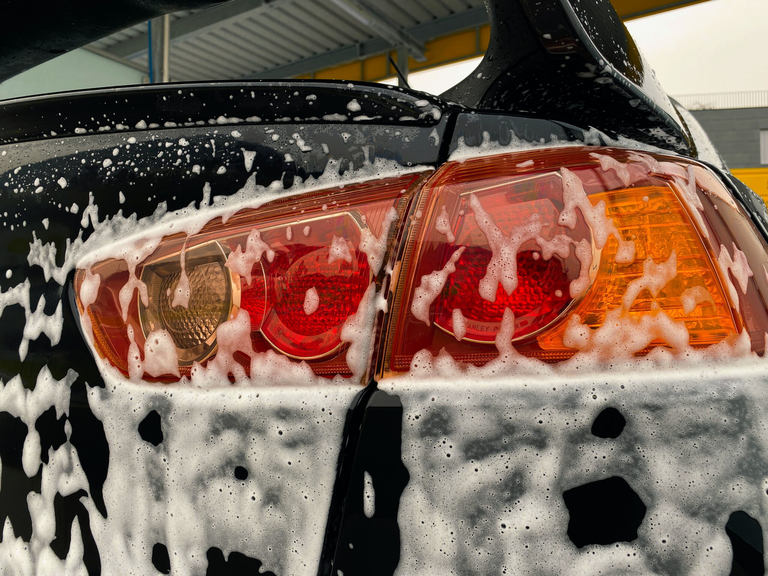 Rear light of a black car covered in soap from a mobile valeting service