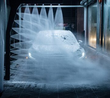 A light coloured car driving through the jets of an automatic carwash with its side lights shining through the foam