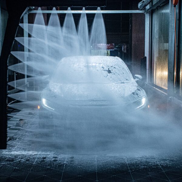 A light coloured car driving through the jets of an automatic carwash with its side lights shining through the foam